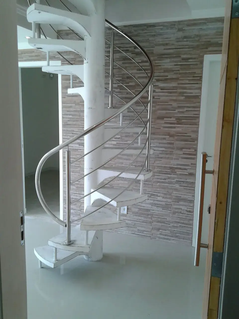 Escada caracol residencial com corrimão curvo em aço inox e degraus claros